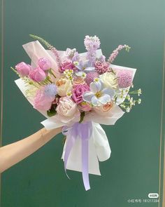 a bouquet of flowers is being held up by someone's hand in front of a green wall