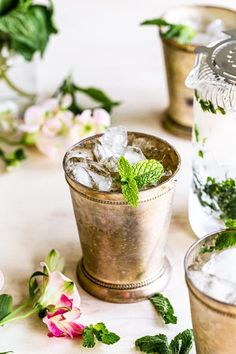 three glasses filled with ice and mint on top of a white table next to flowers