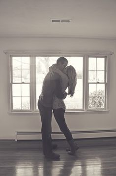 a man and woman are kissing in front of a window with their arms around each other