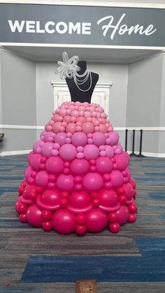 a dress made out of balloons sitting on top of a carpeted floor in front of a welcome home sign