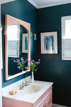 a bathroom with blue walls, pink vanity and flowers in vase on the sink counter