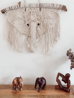 three small figurines sitting on top of a wooden shelf next to a wall hanging