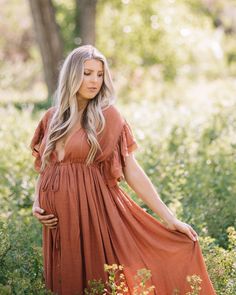 a pregnant woman in an orange dress standing in tall grass