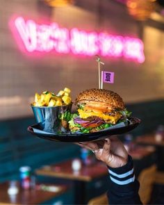 a person holding a plate with a hamburger and fries on it in front of a neon sign