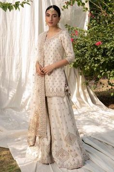 a woman standing in front of a white backdrop wearing a long dress and shawl