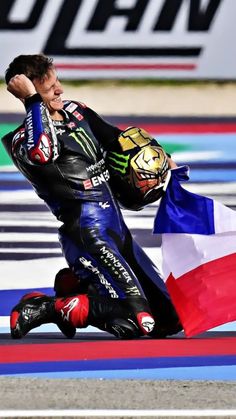 a man riding on the back of a motorcycle next to a red white and blue flag