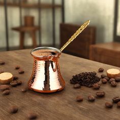 there is a small copper cup on the table with coffee beans around it