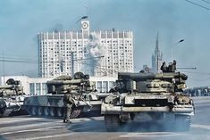 tanks are lined up on the street in front of tall buildings with towers behind them