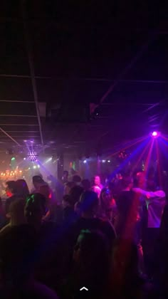 a group of people dancing in a dark room with lights on the ceiling and floor