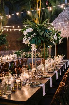 a table set up with white flowers and greenery for an outdoor wedding reception at night