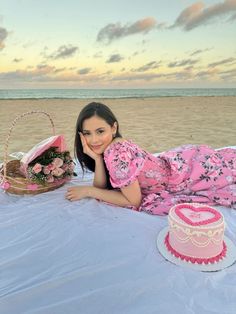 a woman laying on the beach next to a cake and basket with flowers in it