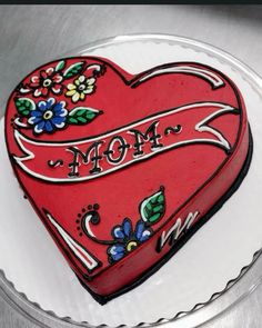 a decorated heart shaped cake on a plate with the word mom painted on it's side