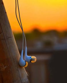 two ear buds attached to a wooden pole with the sun setting in the back ground