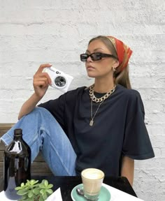 a woman sitting on a bench with a camera and coffee cup in front of her