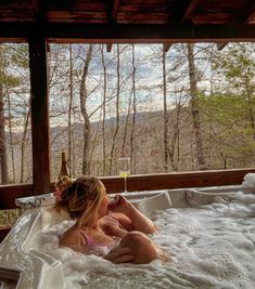 two women sitting in an outdoor hot tub on a deck overlooking the woods and mountains