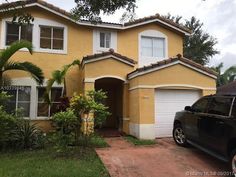 a car is parked in front of a house with palm trees and bushes around it