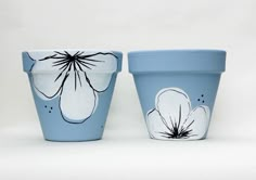 two blue flower pots sitting next to each other on a white surface with flowers painted on them