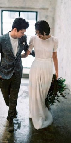 a man and woman are walking together in the rain holding hands while they hold flowers