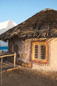 a hut with thatched roof next to the ocean and mountain range in the background