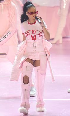 a woman in pink outfit and knee high boots walking on runway with other people behind her