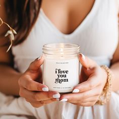 a woman holding a candle with the words i love you mom on it in front of her