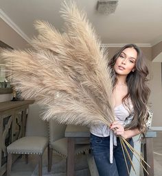 a beautiful woman holding a bunch of dried flowers in front of a dining room table