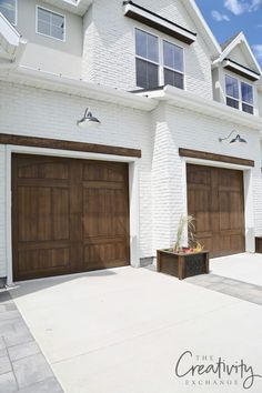 two brown garage doors on the side of a white brick building with an attached planter