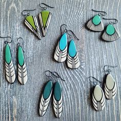 several pairs of earrings are displayed on a wooden surface, including one with green and white feathers