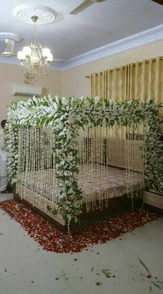 a bed covered in white flowers and greenery next to a chandelier hanging from the ceiling