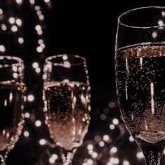 three wine glasses filled with champagne on top of a table next to lights and confetti