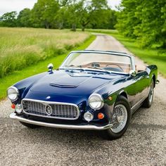 an old blue sports car parked on the side of a road in front of some trees