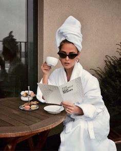 a woman sitting at a table reading a book and holding a coffee cup in her hand