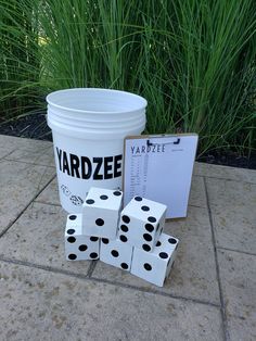 a bucket and four dices sitting on the ground next to a sign that says yardze