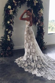 a woman standing in front of a floral arch wearing a wedding dress with an open back