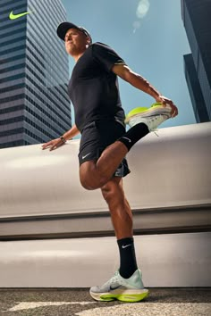 a man in black shirt and shorts holding a tennis racquet next to tall buildings