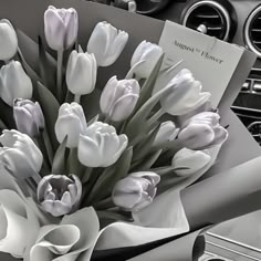 a bouquet of white tulips sitting on top of a car dashboard