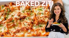 a woman standing in front of a baking dish filled with baked ziti and vegetables