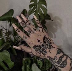 a person's hand with tattoos on it and some green plants in the background