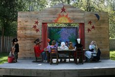 children are sitting at a table in front of a wooden structure with stars on it