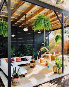 an outdoor living area with hanging plants and couches in the middle, surrounded by greenery