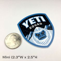 a coin sitting next to a yet squad sticker on top of a white surface