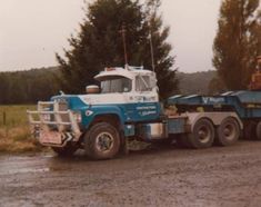 a blue and white tow truck parked on the side of a road next to trees