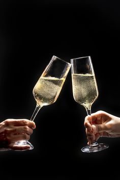 two people toasting with champagne glasses in front of a black background and one person holding out their hands