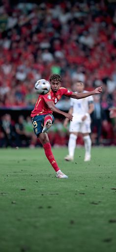 a young man kicking a soccer ball on top of a field with people in the stands watching