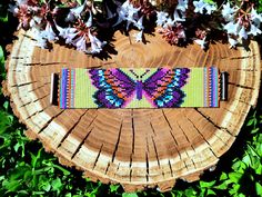 a colorful butterfly bracelet sitting on top of a piece of wood next to white flowers