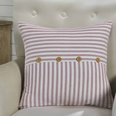 a red and white striped pillow with gold buttons on the front, sitting in a chair