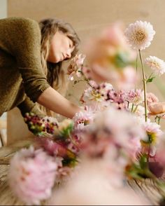 a woman arranging flowers in a vase on a table