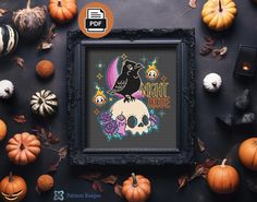 a cross stitch pattern in a frame surrounded by pumpkins and other halloween decorations on a table