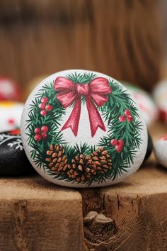 a painted rock with a red bow and pine cones on it sitting on a wooden table