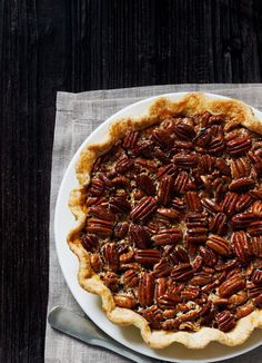 a pecan pie sitting on top of a white plate next to a knife and fork